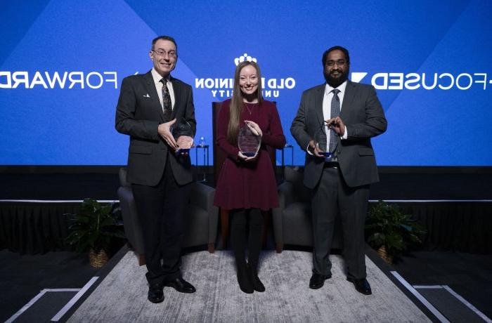 Three people holding awards in front of a screen that reads "forward-focused" 